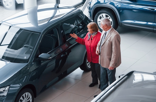 Alter Mann in formeller Kleidung, der Frau bei der Wahl des Automobils unterstützt.