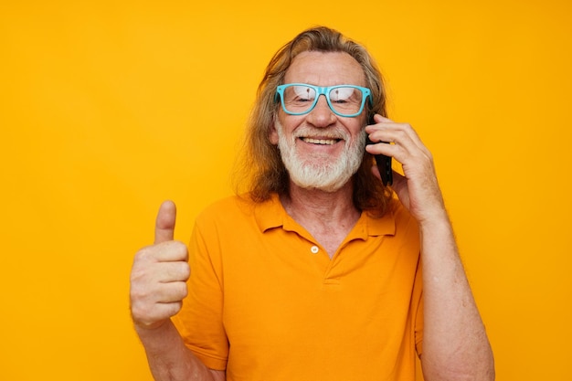 Alter Mann mit blauer Brille, gelbes Hemd, der am Telefon telefoniert, beschnittene Ansicht