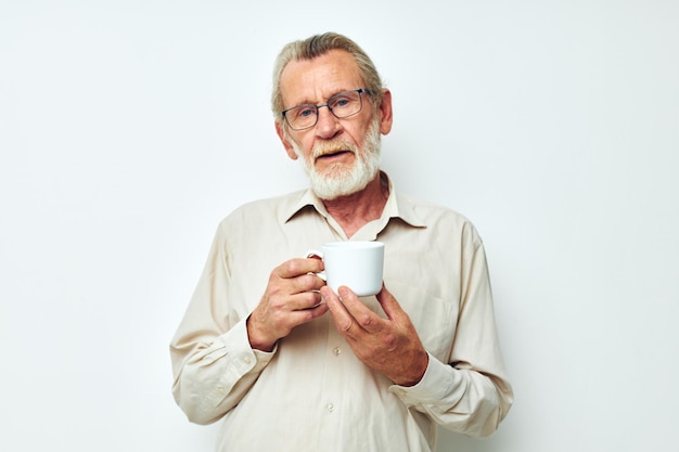 Alter Mann mit Brille mit einem Becher auf weißem Hintergrund und einem weißen Hemd