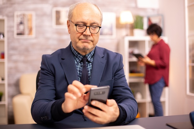 Alter Mann mit neuer Technologie im gemütlichen Haus. Er hat ein Smartphone in der Hand