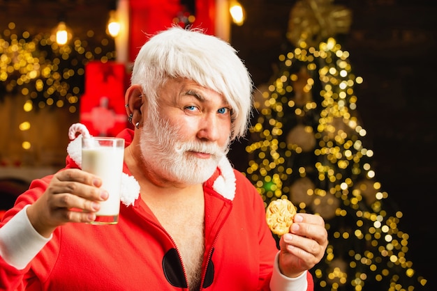 alter Mann mit weißen Haaren im Weihnachtsmannkostüm, das Milch und Keks hält