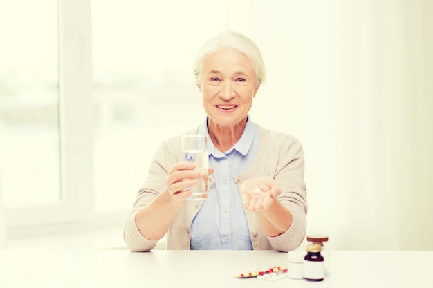 alter, medizin, gesundheitswesen und personenkonzept - glückliche seniorin mit pillen und glas wasser zu hause