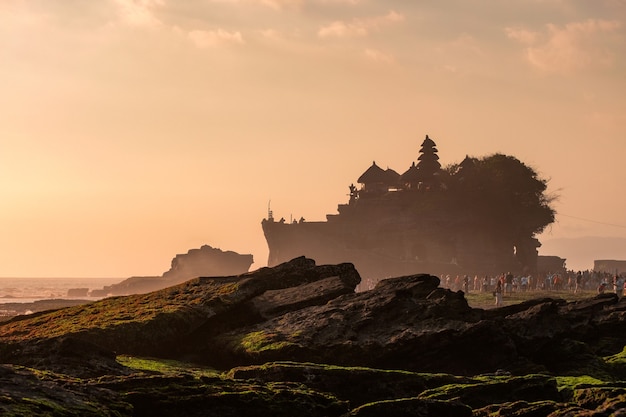 Foto alter tempel tanah lot mit touristen an der küste bei sonnenuntergang in indonesien