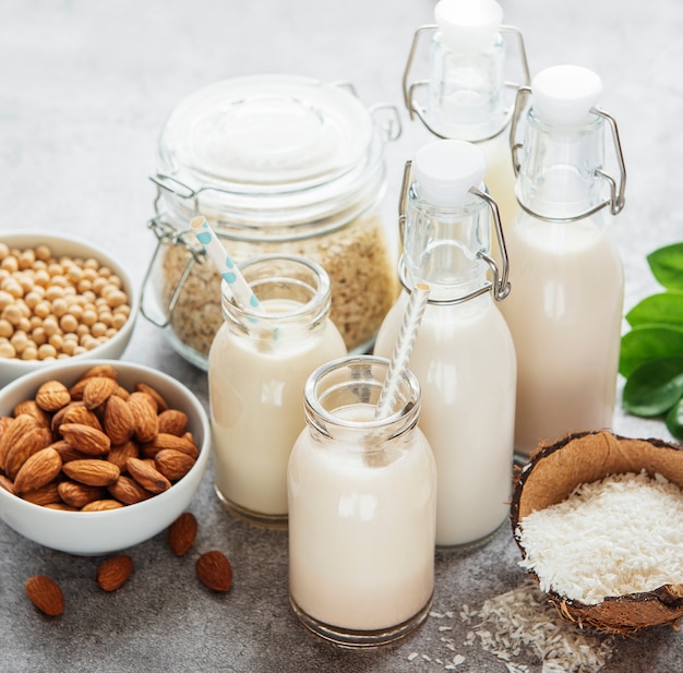 Alternative Arten von veganer Milch in Glasflaschen auf konkretem Hintergrund. Ansicht von oben