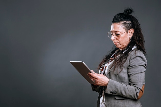 Alternative Frau im Sakkoanzug schaut auf ihr Tablet in Studioaufnahme auf grauem Hintergrund