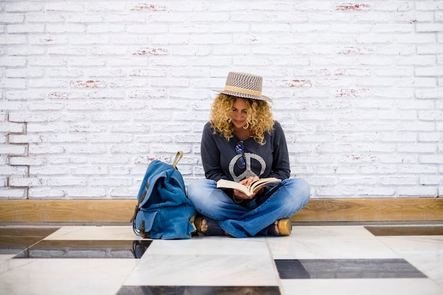 Alternative trendige Reiseleute Lebensstil schöne lockige Mode erwachsene Frau setzen sich auf den Boden und lesen ein Buch mit ihrem blauen Rucksack nera sie