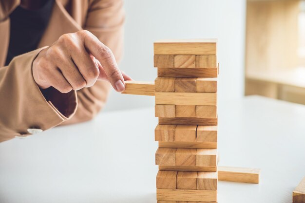 Alternativer Risikoplan und -strategie zum Gewinnwachstum im Geschäft Junge intelligente Geschäftsfrau spielt das Holzspiel Hände des Vorstandsvorsitzenden legen Holzblock auf den Turm