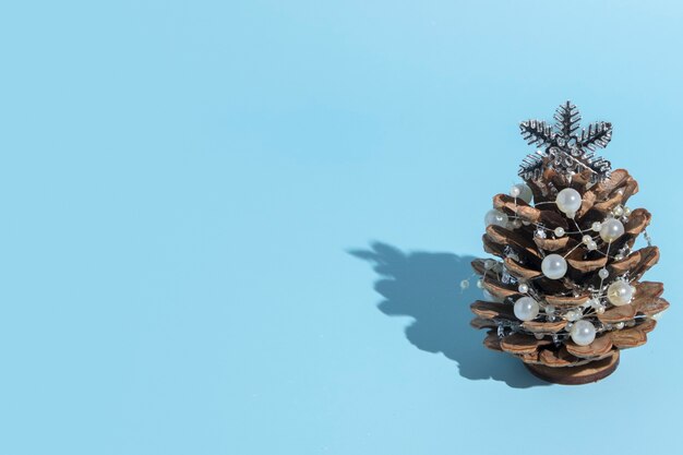 Alternativer Weihnachtsbaum aus Tannenzapfen mit Perlen auf einem blauen Hintergrund mit einem harten Schatten mit Kopienraum in einem minimalistischen Stil für eine Neujahrskarte