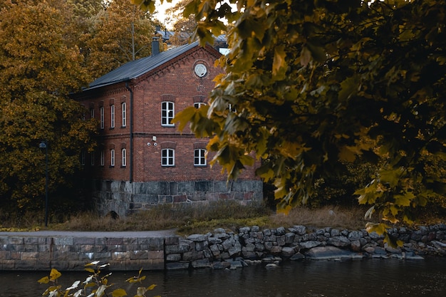 Altes Backsteinhaus auf dem Hintergrund eines Flusses und eines Baums mit Herbstlaub