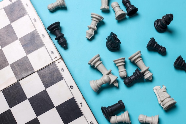 Altes, beschnittenes Schachbrett mit schwarzen und weißen Figuren auf blauem Hintergrund, Draufsicht, flache Lage