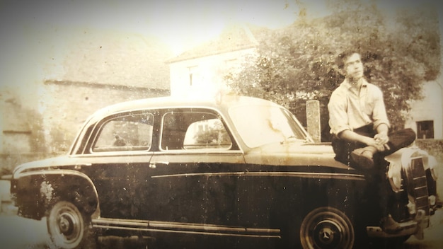 Foto altes foto eines mannes, der auf einem auto sitzt