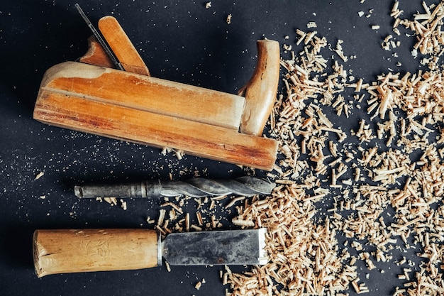 Altes Handflugzeug, Bohrer und Meißel mit Holzspänen auf schwarzem Hintergrund. Altes Handwerkzeug für die Holzbearbeitung. Kopieren, leerer Platz für Text