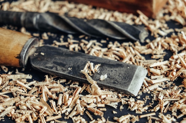 Altes Handflugzeug, Bohrer und Meißel mit Holzspänen auf schwarzem Hintergrund. Altes Handwerkzeug für die Holzbearbeitung. Kopieren, leerer Platz für Text