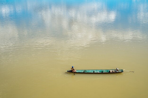 Altes hölzernes Fischerboot im Fluss mit Reflexion des Himmels