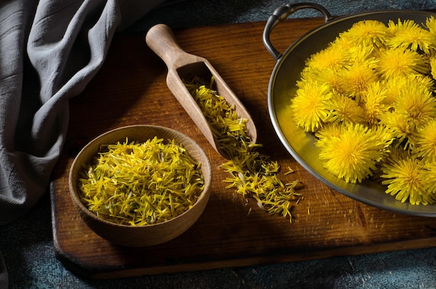 Altes Holzbrett mit Blumen Löwenzahn in Metallplatte und Blütenblätter Löwenzahn. Dunkles Foto. Nahansicht.