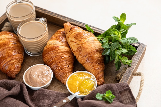 Altes Holztablett mit knusprigen Croissants, Marmelade, Schokoladencreme und Kaffee