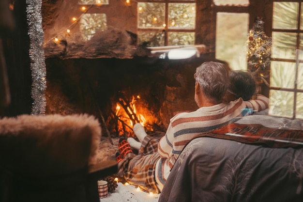 Altes kaukasisches Ehepaar, das Freizeit zu Hause verbringt Liebevoller romantischer Ehemann und Ehefrau, die sich entspannen, während sie während der Winterweihnachtsferien auf den brennenden Kamin schauen