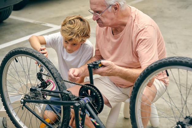 Alto ángulo de anciano serio y nieto en ropa deportiva durante la reparación de la rueda de la bicicleta