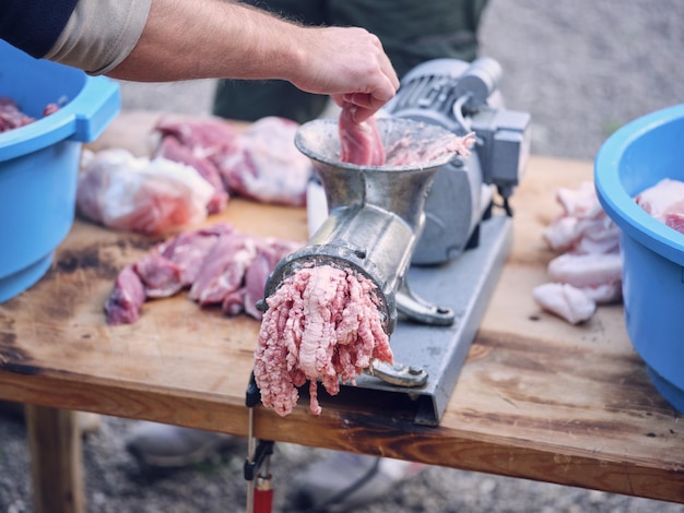 Alto ángulo de carnicero masculino sin rostro poniendo carne de cerdo fresca en una picadora de carne de metal mientras prepara carne picada para chorizo en un matadero tradicional español