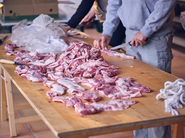 Alto ángulo de cosecha carniceros masculinos irreconocibles con ropa informal tallando carne de cerdo cruda fresca con cuchillo parado en una mesa de madera en un matadero tradicional en Mallorca