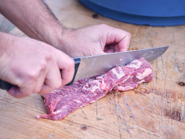 Alto ângulo de açougueiro masculino anônimo cortando carne de porco crua com faca afiada na mesa de madeira à luz do dia
