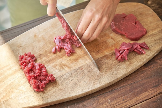 Alto ângulo de chef profissional irreconhecível no processo de corte de carne crua na tábua com faca enquanto cozinha bife tártaro