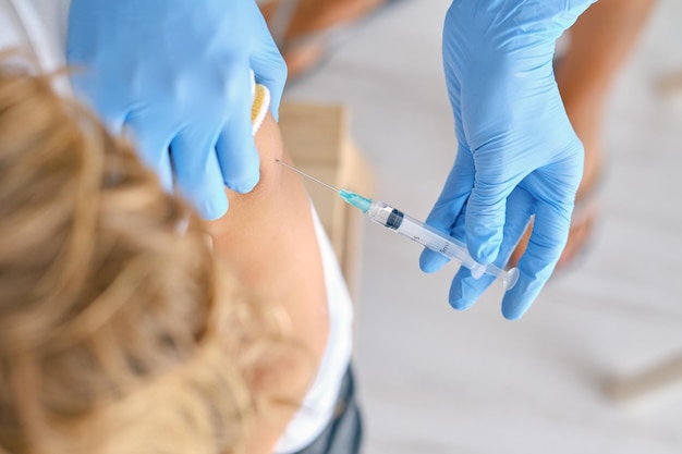 Alto ângulo de colheita médica irreconhecível em luvas de látex injetando vacina contra o coronavírus no ombro do paciente na clínica