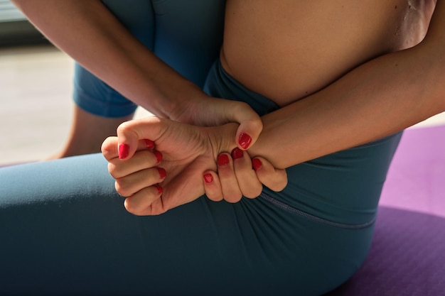 Alto ângulo de corte feminino irreconhecível em roupas esportivas apertando as mãos enquanto pratica Marichyasana durante a sessão de ioga