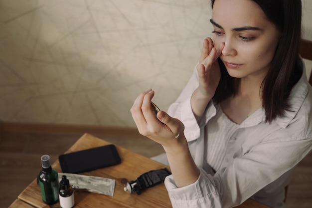 Alto ângulo de mulher delicada aplicando delicadamente creme facial durante tratamento de beleza de cuidados com a pele