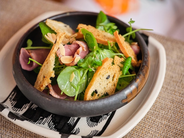 Alto ângulo de salada apetitosa com presunto de espinafre e croutons em tigela de madeira colocada sobre pano na mesa do restaurante