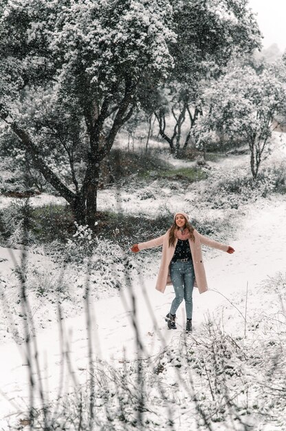 Alto ángulo de mujer caminando con los brazos extendidos a lo largo del camino nevado y disfrutando de un paseo en el bosque en invierno