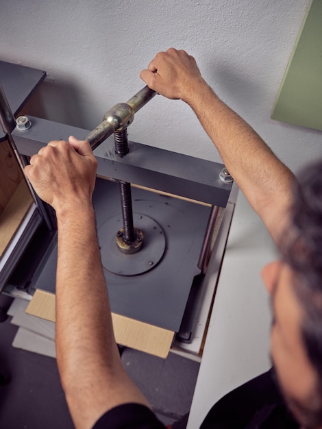 Alto ángulo de trabajador masculino anónimo que usa una máquina mientras trabaja en un taller de madera con equipo durante el trabajo