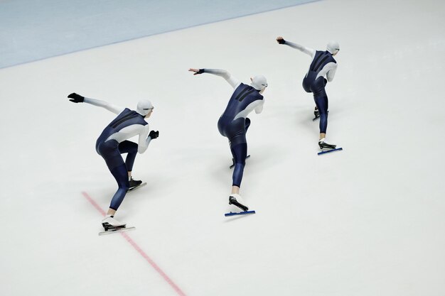 Alto ángulo de tres jóvenes en uniforme deportivo y patines moviéndose a lo largo de la pista de hielo