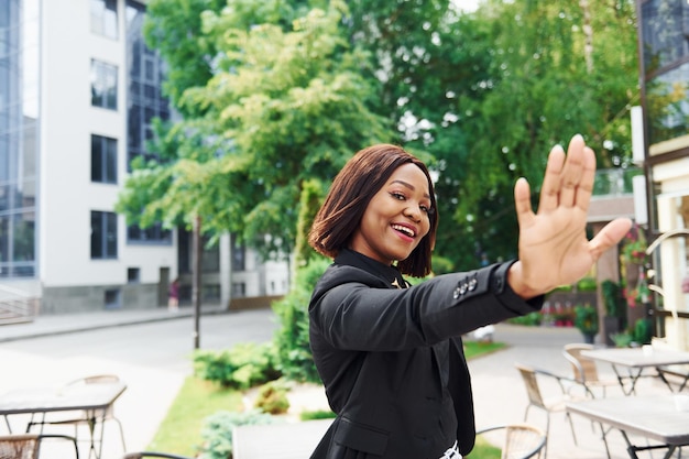 Alto cinco gesto Joven mujer afroamericana en ropa de moda al aire libre en la ciudad cerca de árboles verdes y contra el edificio de negocios