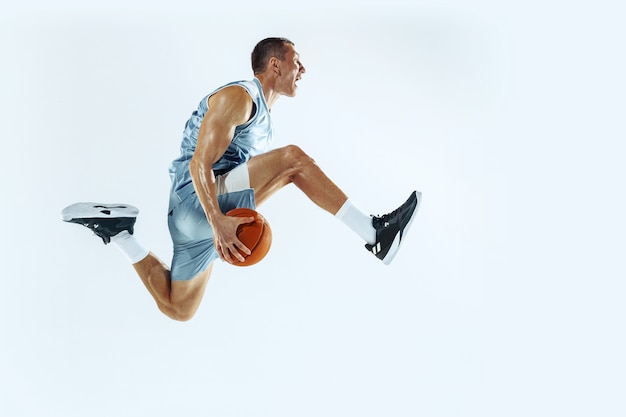 Alto vuelo. Joven jugador de baloncesto caucásico del equipo en acción, movimiento en salto aislado sobre fondo blanco. Concepto de deporte, movimiento, energía y estilo de vida dinámico y saludable. Entrenando, practicando.