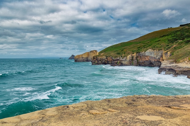 Altos acantilados arenosos y olas del océano Pacífico en Tunnel Beach, Nueva Zelanda