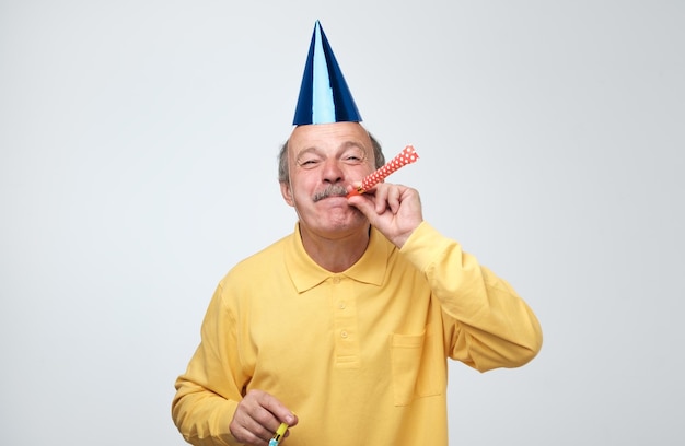 Altos hombre vestido con gorro de fiesta mientras sopla la bocina