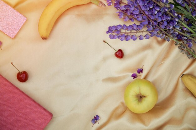 Altramuces flores púrpura cuaderno manzana cereza plátano decoraciones sobre fondo dorado Picnic de verano Bienestar cercanía a la naturaleza concepto de autodescubrimiento