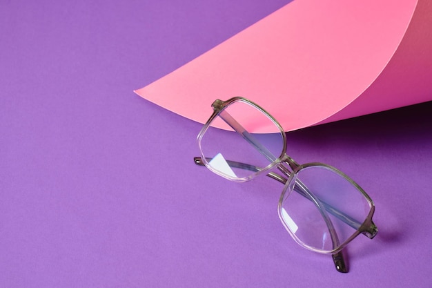 Alugue óculos em fundo geométrico rosa e roxo, espaço de cópia de armações de óculos da moda, papel enrolado e óculos da moda