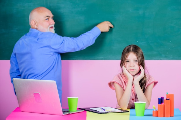 Una alumna aburrida, una niña con un tutor, estudia en un cuaderno, un maestro maduro, ayuda a una niña de la escuela, una lección escolar en línea, escribe un ensayo, una nueva tecnología en el aprendizaje de la educación en línea, de regreso a la escuela.