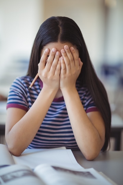 Alumna estresada haciendo cubriéndose la cara en el aula