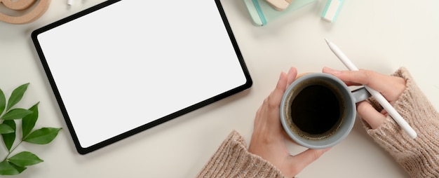 Alumna manos sosteniendo la taza de café mientras trabaja con simulacro de tableta en la mesa de estudio