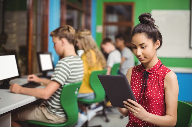 Foto alumna con tableta digital mientras otros estudiantes estudian en la computadora en el aula