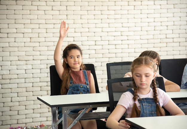 Las alumnas de la escuela primaria levantan la mano para preguntarle a la maestra de clase