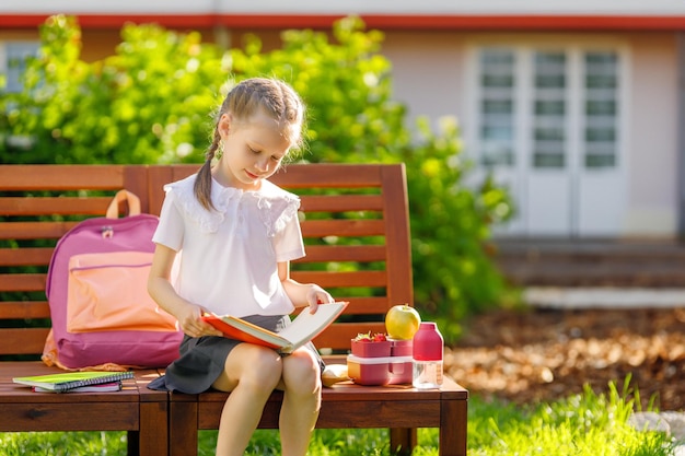 Foto alumno con caja de almuerzo niña con mochilas está comiendo fruta cerca del edificio al aire libre comienzo de las lecciones