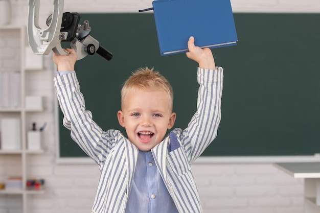 Alumno de colegial emocionado con microscopio y libro de regreso a la escuela niño en la escuela el niño está aprendiendo en c