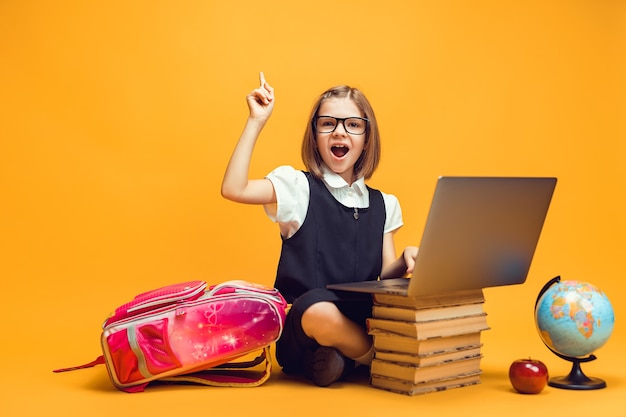 Alumno emocional se sienta detrás de la pila de libros con la computadora portátil levanta la mano con el dedo índice de educación infantil