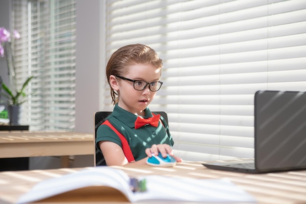 El alumno de la escuela está estudiando la educación en el hogar en línea para niños a distancia aprendiendo a un niño lindo usando una computadora portátil ed