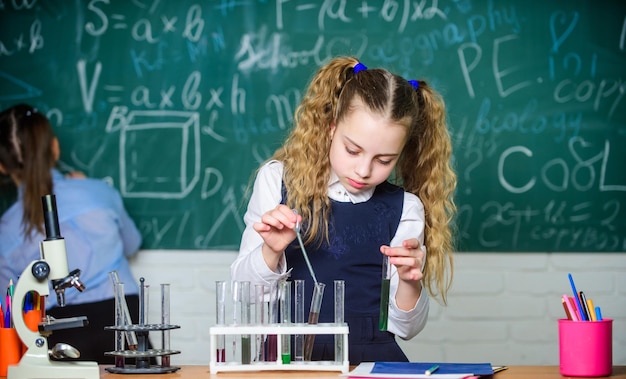 Alumno de la escuela estudia líquidos químicos Lección de química escolar Tubos de ensayo con sustancias Futuro microbiólogo Cristalería de laboratorio Laboratorio escolar Chica estudiante inteligente realizar experimento escolar