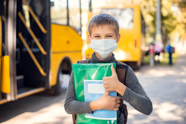 Alumno de la escuela en máscara médica sosteniendo materiales de aprendizaje